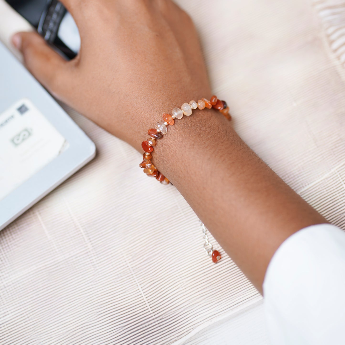 Hand wearing a beaded bracelet using a laptop on a light surface