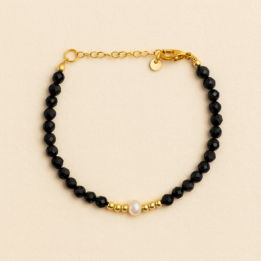 Bracelet with black beads, gold chain, and pearl on a beige background      
