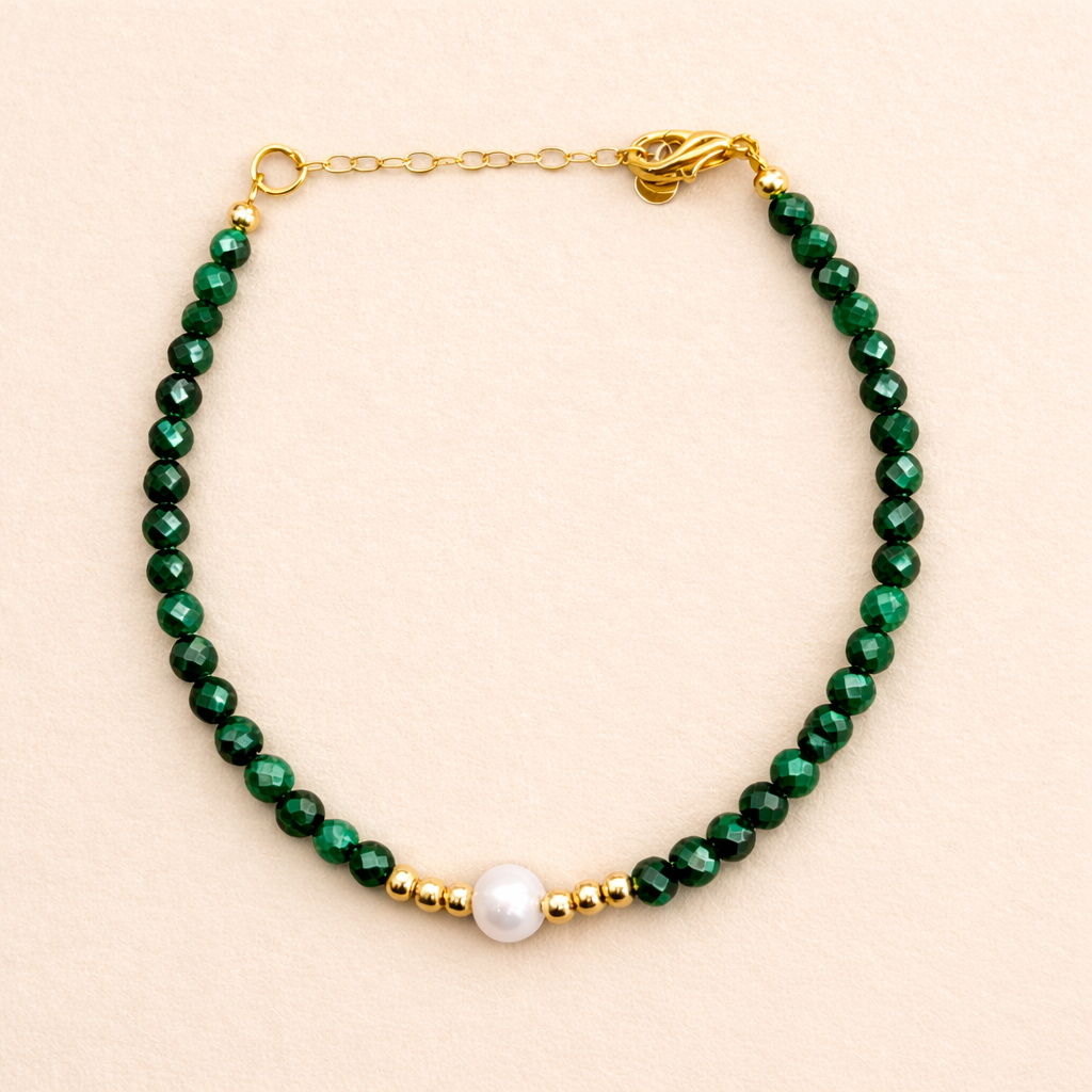 bracelet with green beads, gold chain and pearl on a beige colour background