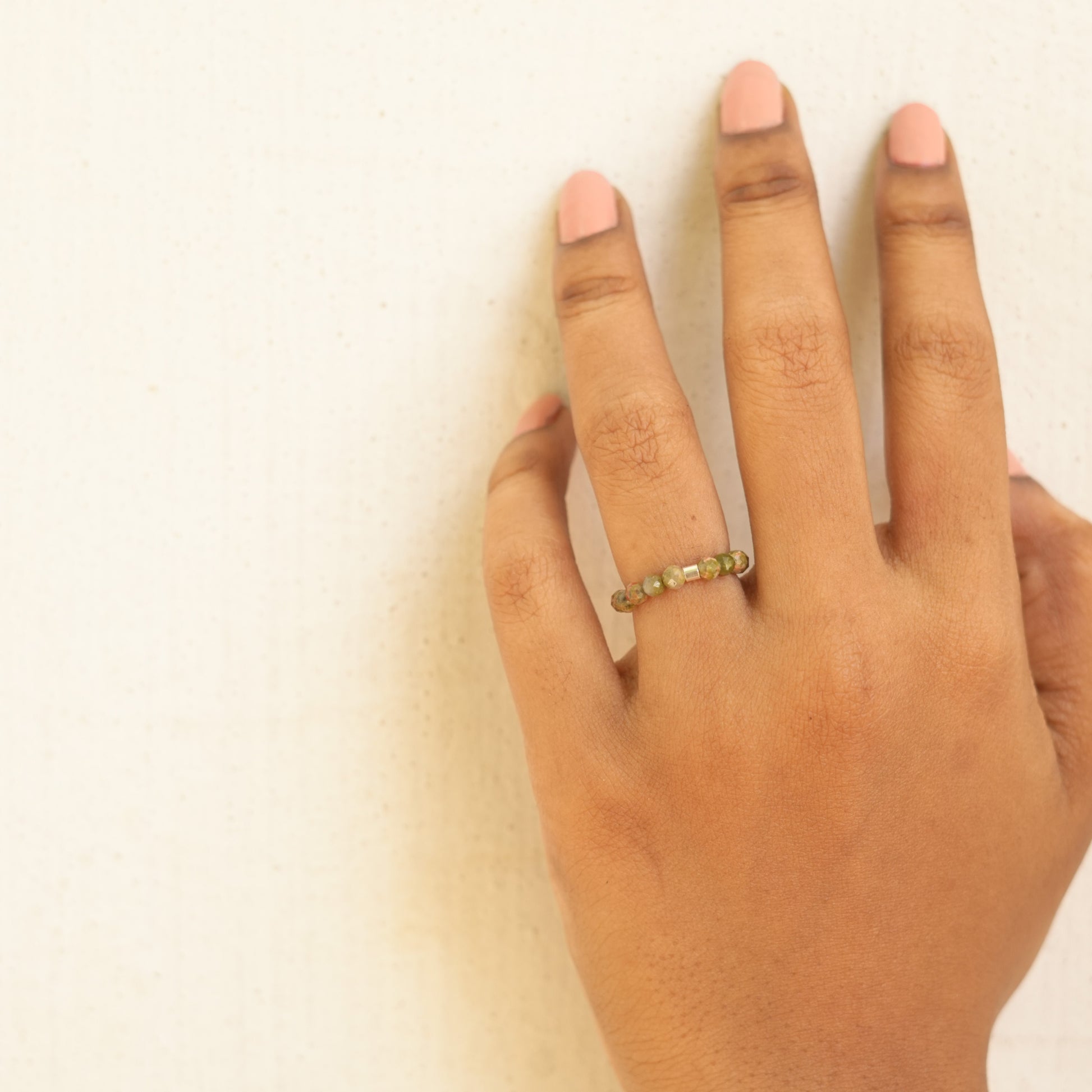 light green beaded ring on a finger with a white background